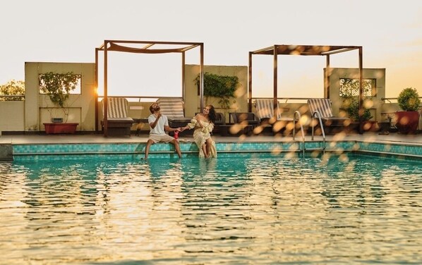 A rooftop pool area with lounge chairs and a pergola structure.