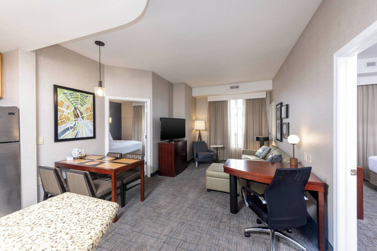 A hotel room with a bed, a desk, a chair, a television, a sofa, and a dining table.