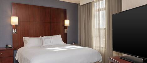 Habitación de hotel con una cama grande, dos lámparas de noche, un televisor de pantalla plana, una mesita de noche de madera y una ventana con cortinas.