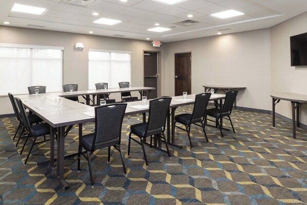 A conference room with multiple tables and chairs, large windows, and a patterned carpet.