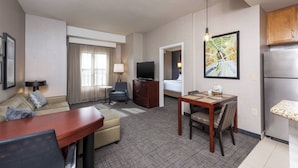 A hotel room with a living area, a dining table, a sofa, a TV, and a kitchen area. - Residence Inn Midland Marriott (Midland)