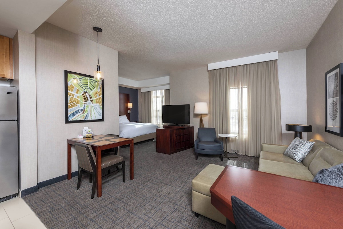 A hotel room with a bed, a TV, a desk with a chair, a sofa, and a dining table.