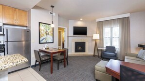 A modern hotel room with a kitchen, dining area, and living room. It includes a flat-screen TV, a fireplace, and a comfortable seating area. - Residence Inn Midland Marriott (Midland)