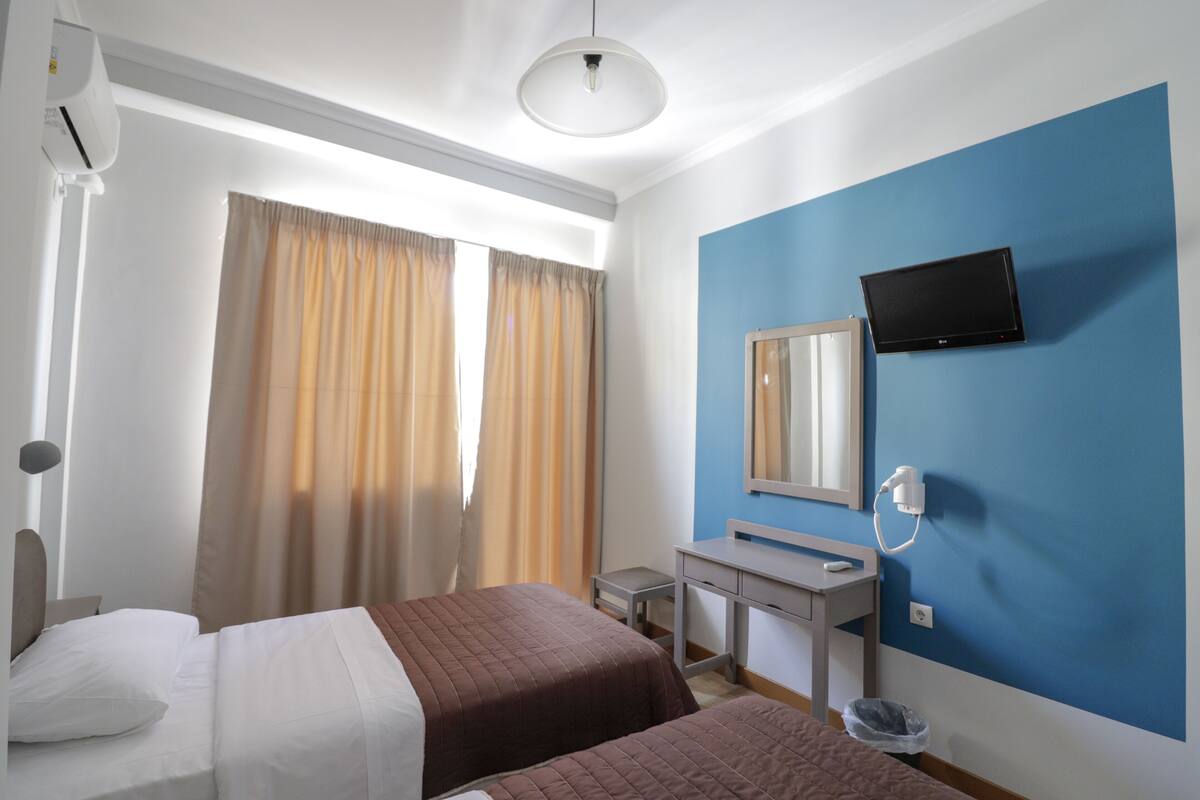 A hotel room with two beds, a desk, a mirror, a TV, and a window with curtains.