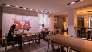 Une salle de réunion moderne, dotée de tables et de chaises en bois, d’une grande fresque murale et d’un grand miroir.