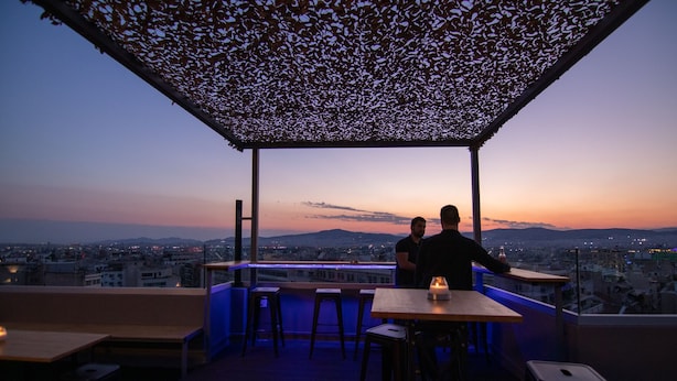 Une terrasse sur le toit offrant une vue sur la ville au crépuscule, avec une pergola et des sièges de bar.
