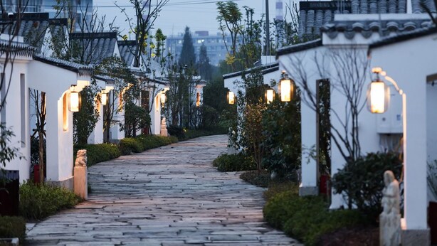 A traditional-style pathway leading to a building with white walls and tiled roofs, surrounded by greenery and stone paving. - Dayu Kaiyuan (Shaoxing)