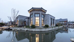 A modern house with a stone facade, large windows, and a pond in front. - Dayu Kaiyuan (Shaoxing)