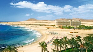 A beachfront hotel with a pool area, beach umbrellas, and palm trees.