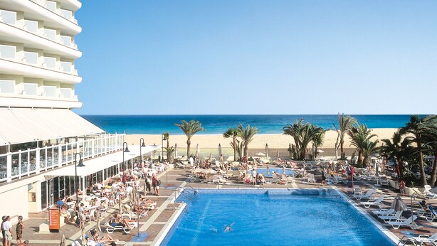 A resort pool area with a clear view of the ocean, lounge chairs, and palm trees.