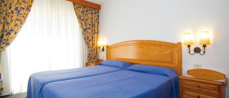 A double bed with a wooden headboard, two bedside lamps, and a wooden nightstand with a drawer.