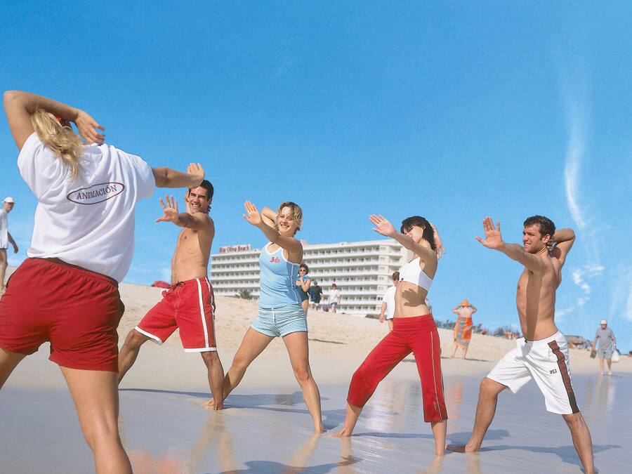 A group of people performing a dance on a beach with a hotel in the background.