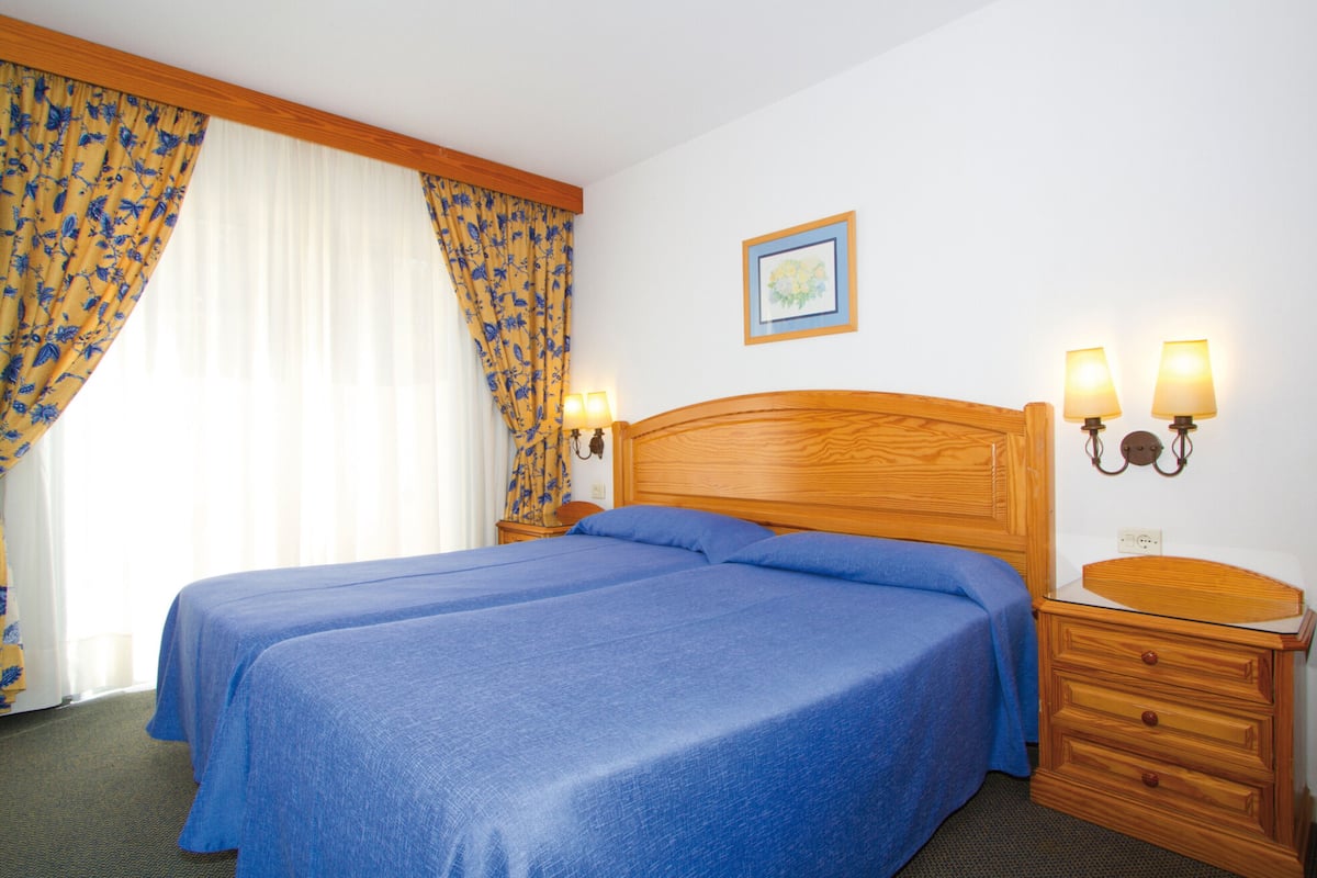 A double bed with a wooden headboard, two bedside lamps, and a nightstand with a mirror.