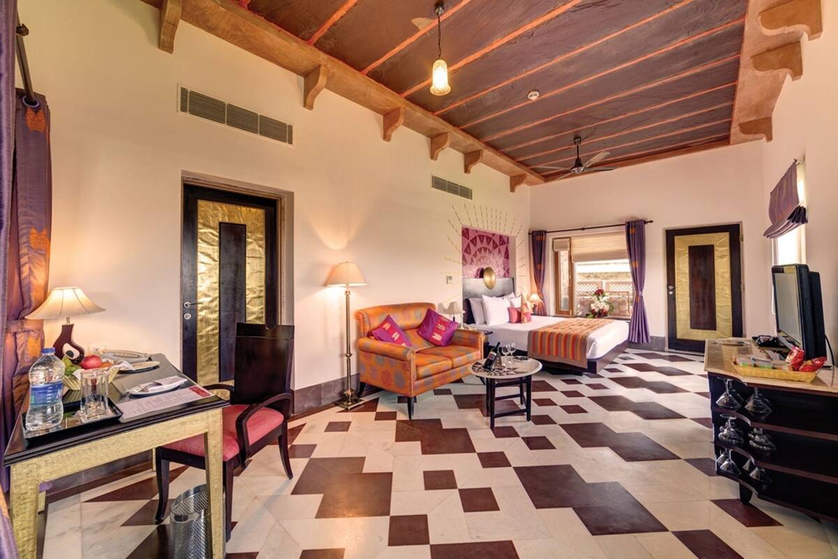 Une chambre d’hôtel avec un sol à carreaux, un lit, un canapé, un bureau avec une lampe et un téléviseur.
