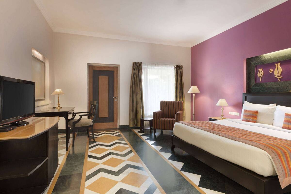 Une chambre d’hôtel comprenant un lit, un bureau avec une télévision, une chaise et une petite table.