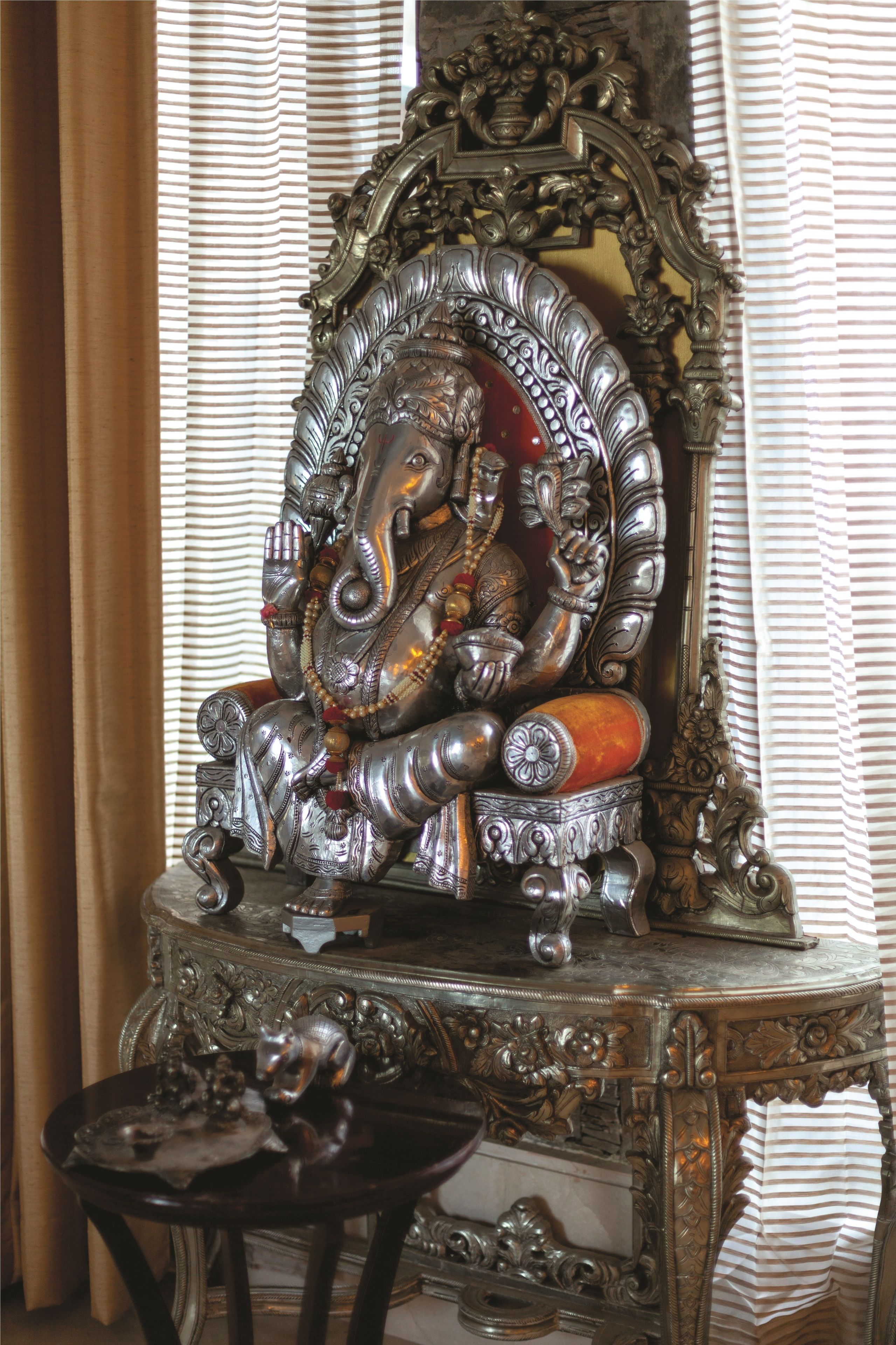 Una estatua de una deidad sobre un soporte decorativo con intrincados grabados, ubicada frente a un espejo con detalles ornamentales.