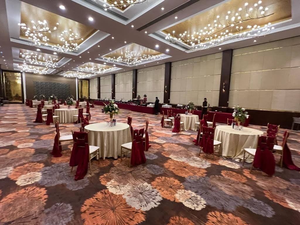 A banquet hall with round tables, red chairs, and a patterned carpet.