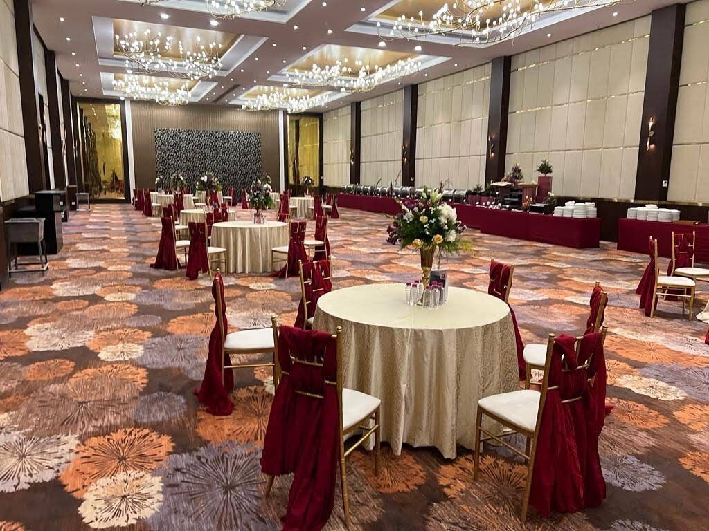 A banquet hall with round tables and red chairs, a floral centerpiece, and a chandelier.
