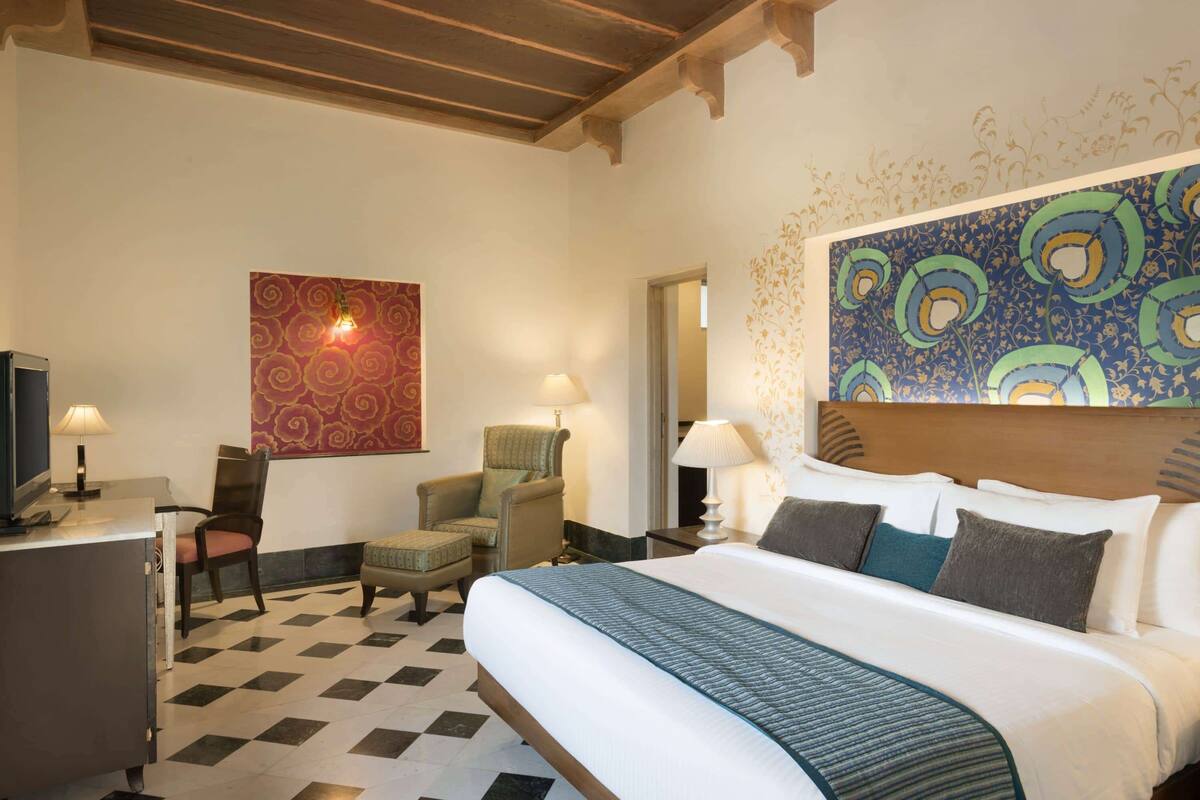 Une chambre d’hôtel avec un grand lit, un bureau avec une lampe, deux fauteuils et un téléviseur.