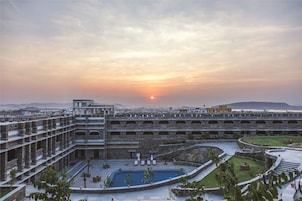 Un edificio de varios pisos con piscina y zona de estar exterior, rodeado de vegetación y vistas al atardecer.