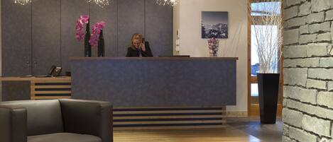 A reception area with a modern design, featuring a reception desk, a seating area with a sofa and ottoman, and decorative elements like orchids and a cityscape painting.