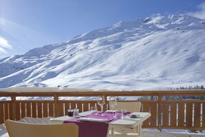 A dining table set with white tableware and a purple table runner, overlooking a snow-covered mountain. - Le Chalet du Mont Vallon Spa Resort (Les Belleville)