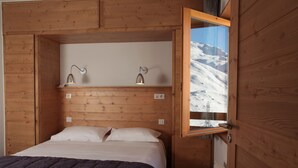 A wooden room with a bed, two wall-mounted lamps, and a window with a snowy mountain view. - Le Chalet du Mont Vallon Spa Resort (Les Belleville)