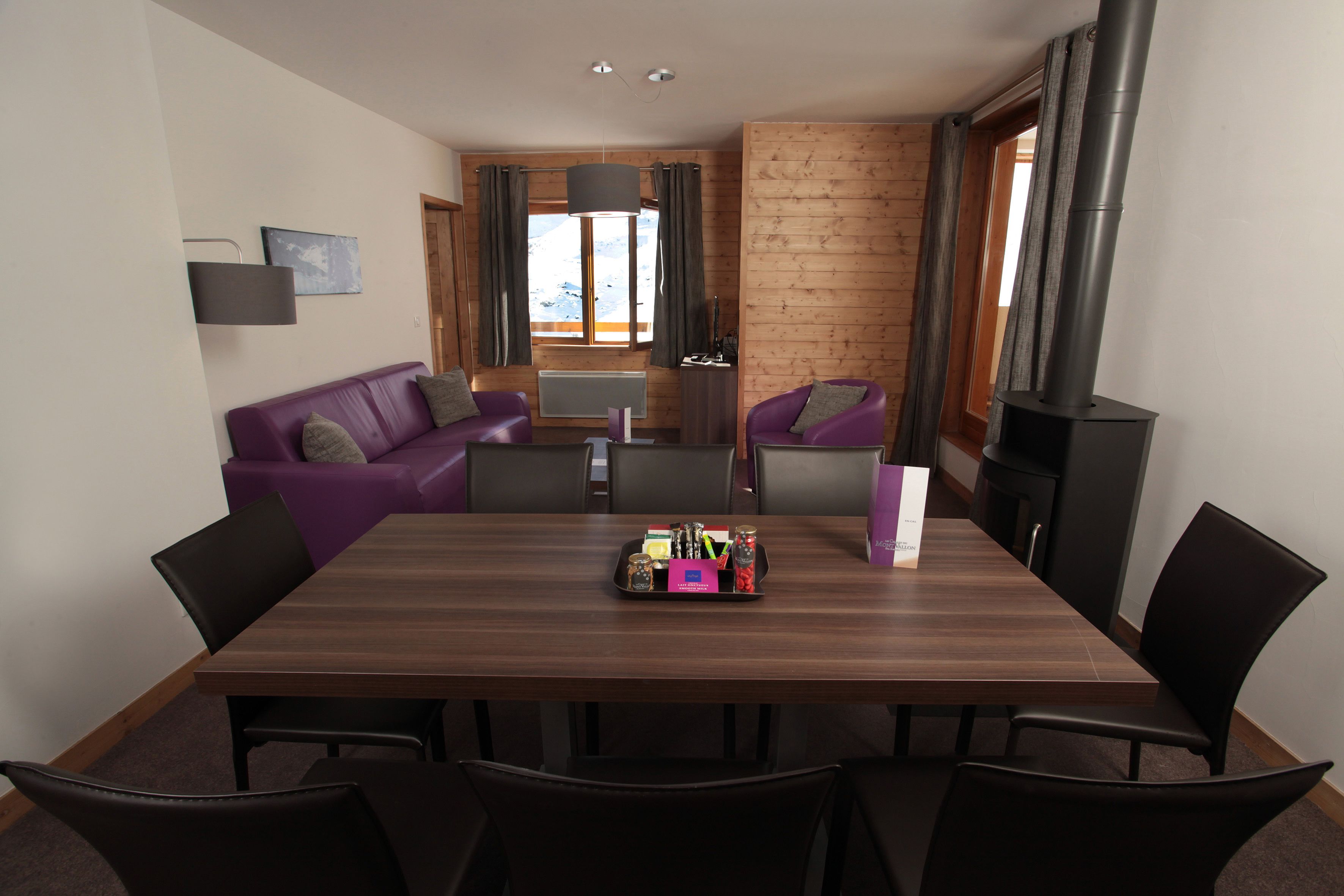 Una sala moderna con una pared de madera, un sofá morado, una mesa de comedor con sillas y una chimenea.