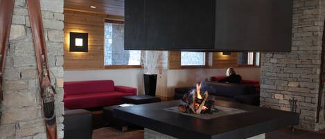 Un salon moderne doté d’une cheminée en pierre, de canapés rouges et d’une échelle en bois appuyée contre un mur de pierre.