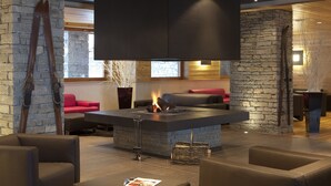A modern lounge area with a stone fireplace, leather seating, and a large TV screen. - Le Chalet du Mont Vallon Spa Resort (Les Belleville)