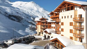 A snow-covered mountain resort with wooden buildings, a parking area, and a clear blue sky. - Le Chalet du Mont Vallon Spa Resort (Les Belleville)