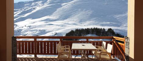 Eine Holzterrasse mit Tisch und Stühlen mit Blick auf eine verschneite Berglandschaft.