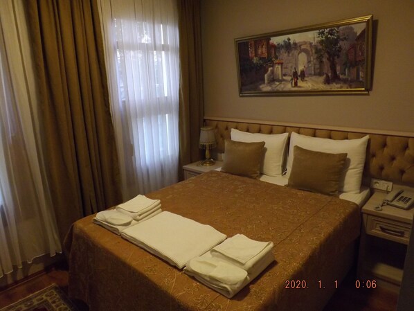 A hotel room with a neatly made bed, a painting on the wall, and a bedside table with a lamp and phone.
