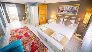 A hotel room with a large bed, a sitting area with a blue chair, a wardrobe, a nightstand with a lamp, and a painting on the wall.