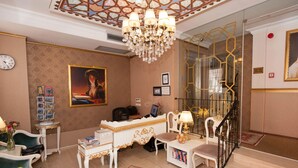 A room with a chandelier, a desk with a computer, a chair, a bookshelf, and a painting on the wall.