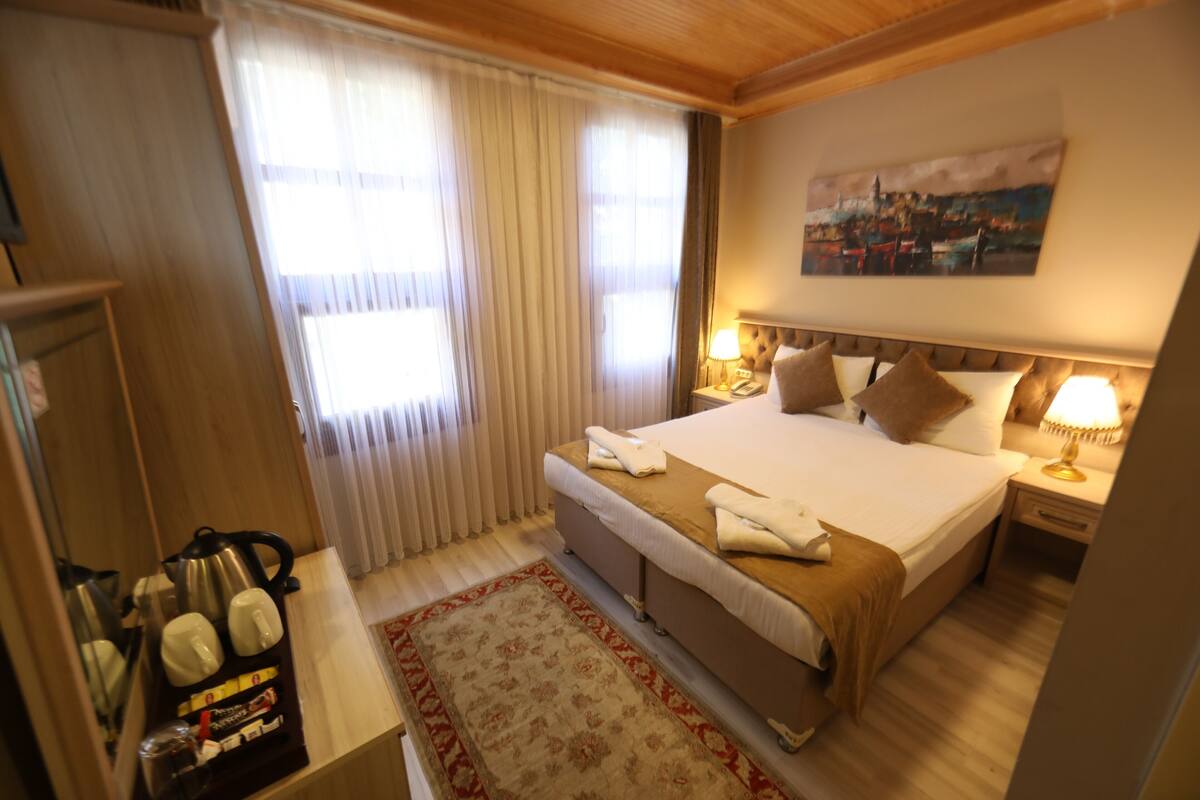 A hotel room with a bed, bedside lamps, a painting on the wall, and a window with curtains.