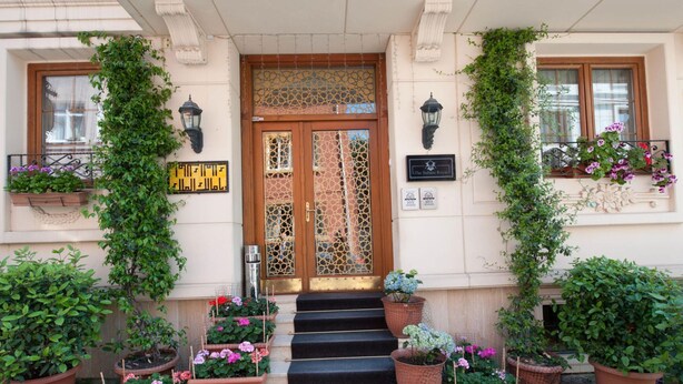 A building entrance with a wooden door, a sign with Arabic script, and potted plants.