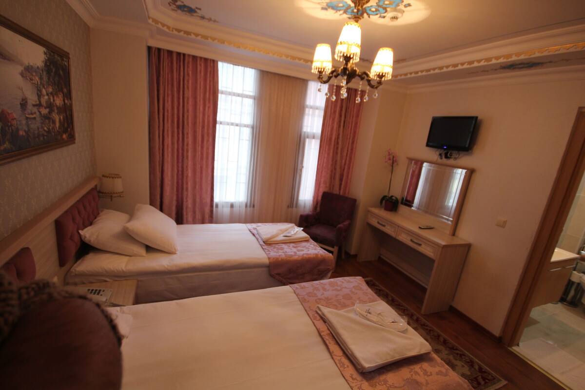 A hotel room with two beds, a desk, a chair, a television, and a large window with curtains.