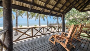 Una terraza de madera con vistas a la playa y palmeras.