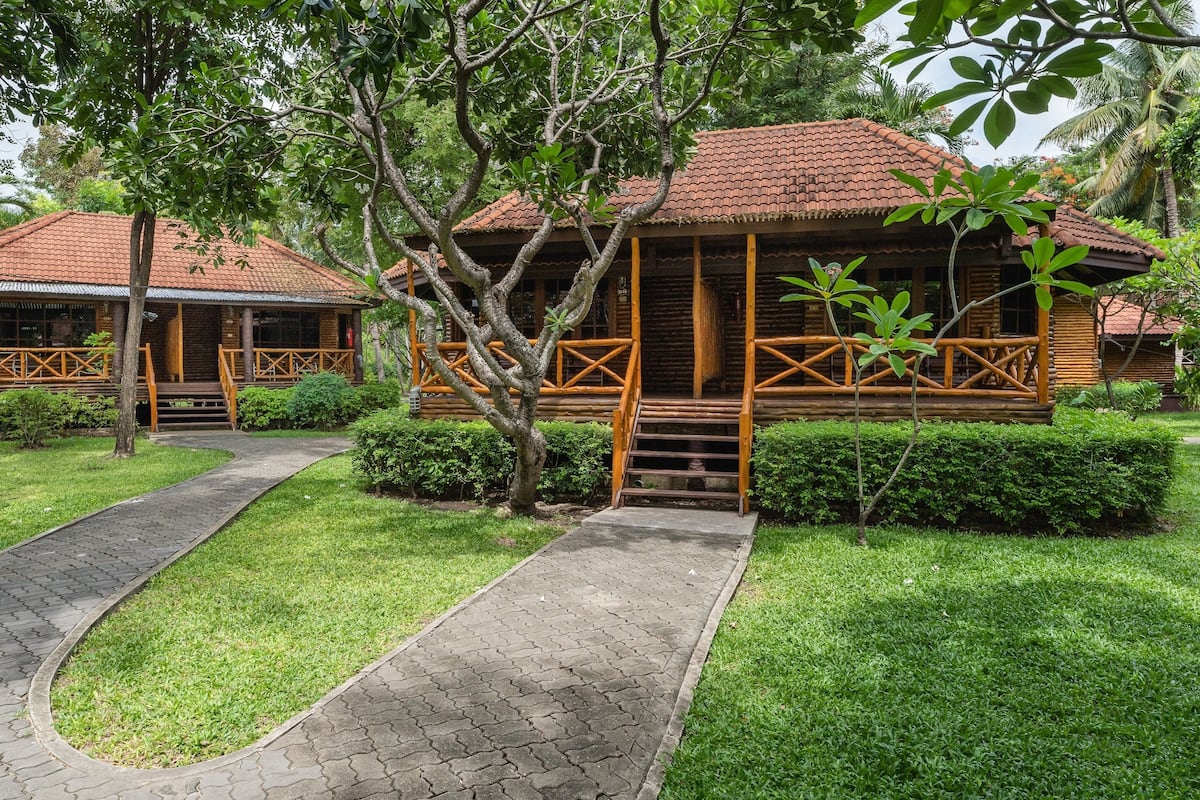 A wooden lodge with a tiled roof, surrounded by lush greenery and a paved walkway.