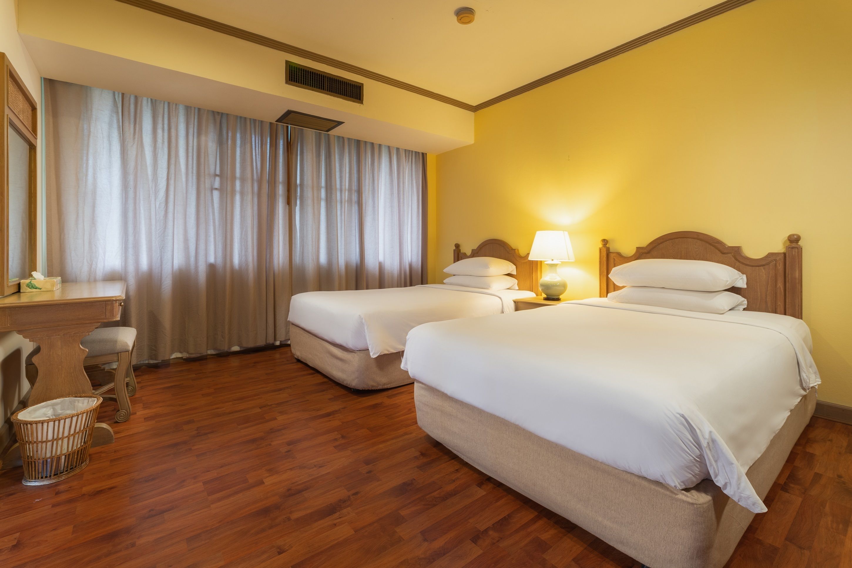 A hotel room with two beds, a desk, a chair, and a window with curtains.