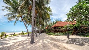 Un resort frente a la playa con palmeras, un sendero de arena y edificios de madera con techos rojos.