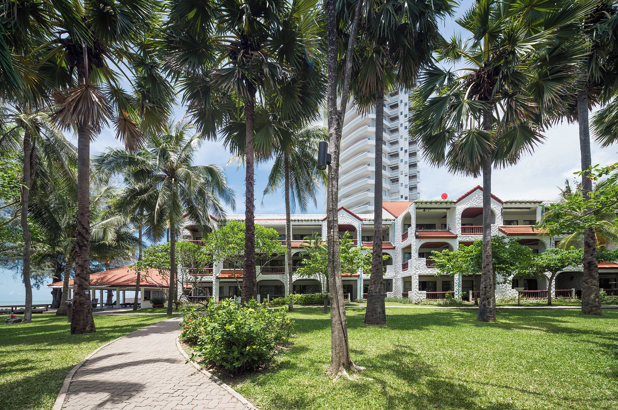 A pathway leading to a building with multiple balconies and a red-tiled roof.