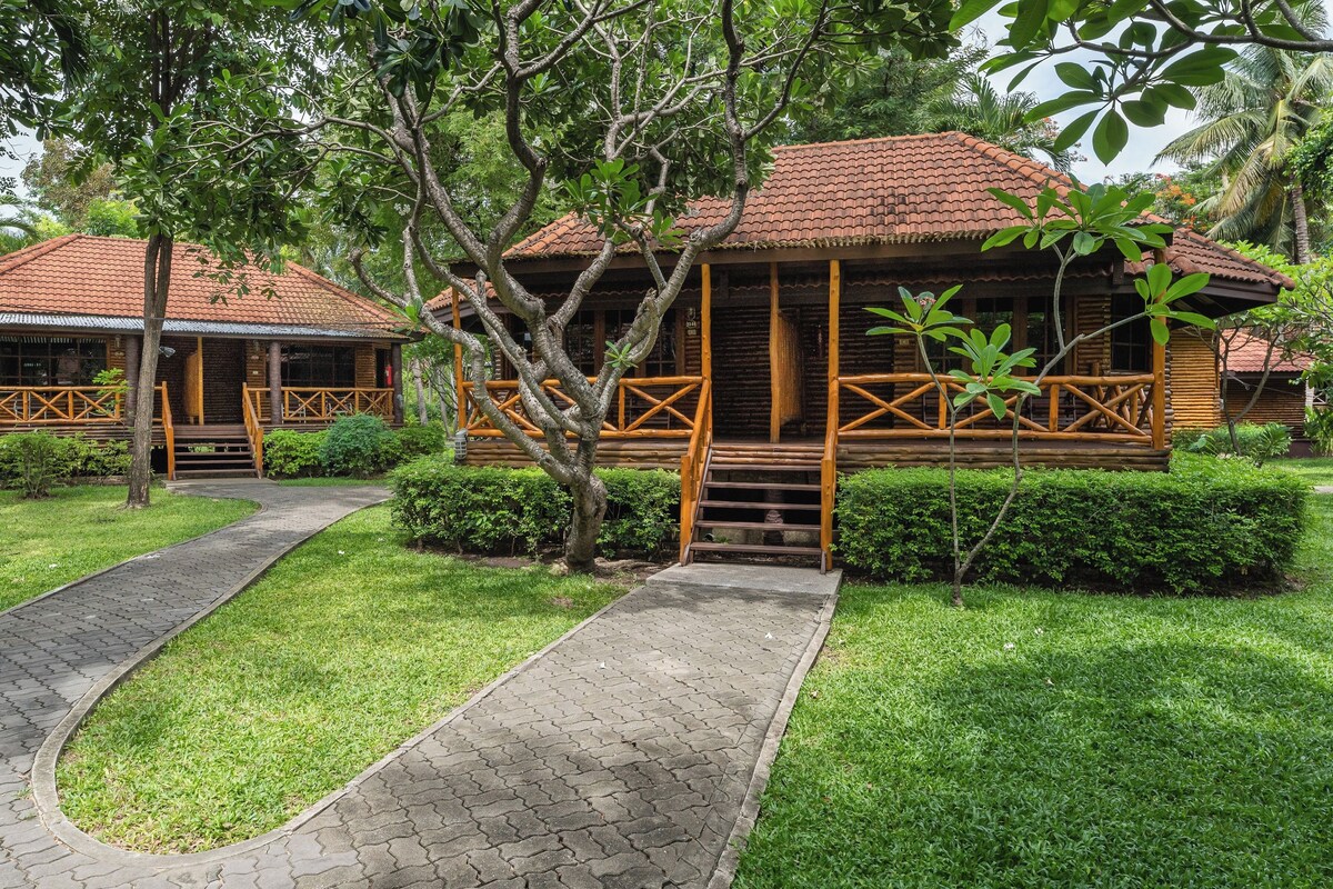 A wooden lodge with a tiled roof, surrounded by lush greenery and a paved walkway.