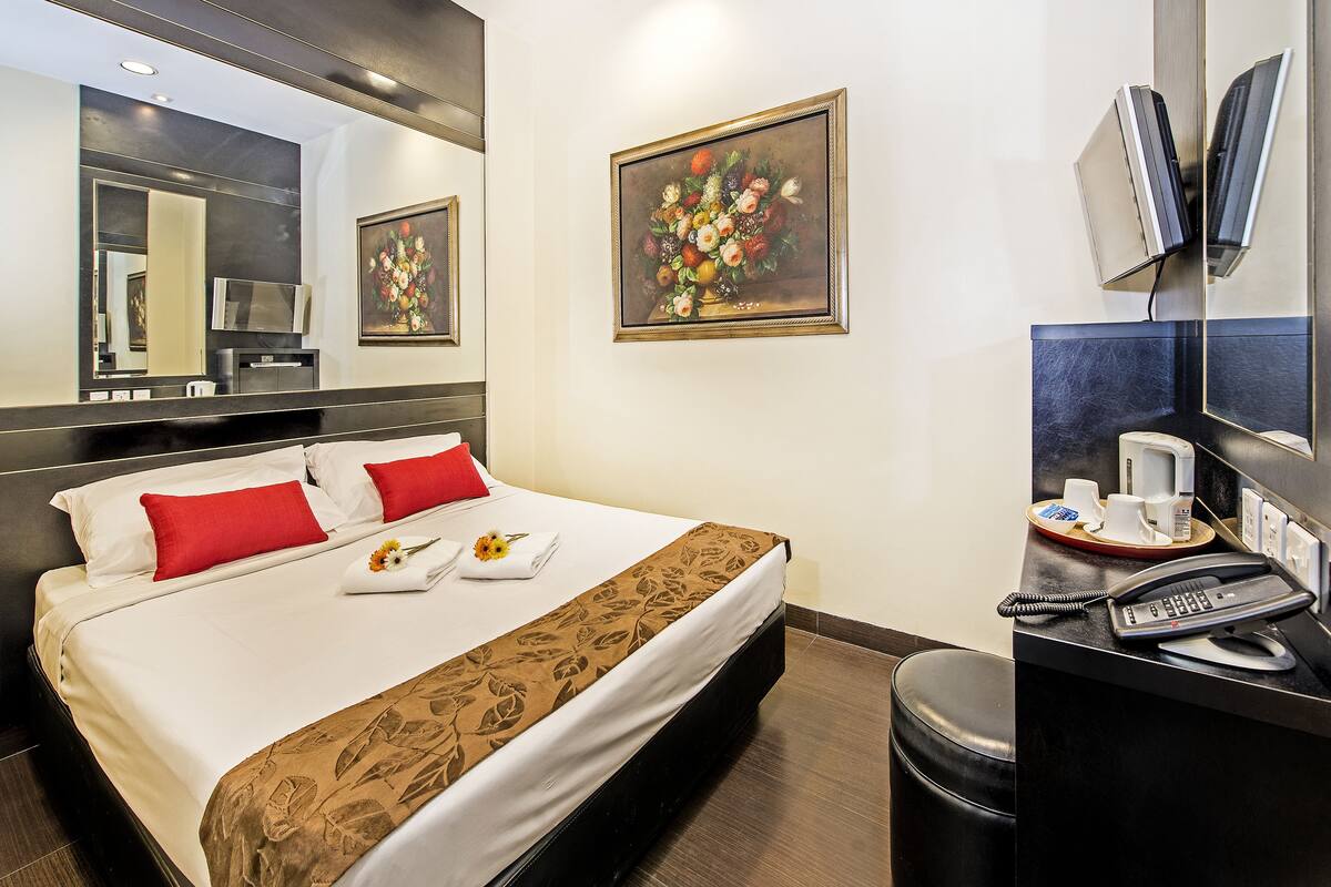 Quarto de hotel com uma cama, uma escrivaninha com telefone, uma cafeteira e um quadro na parede.