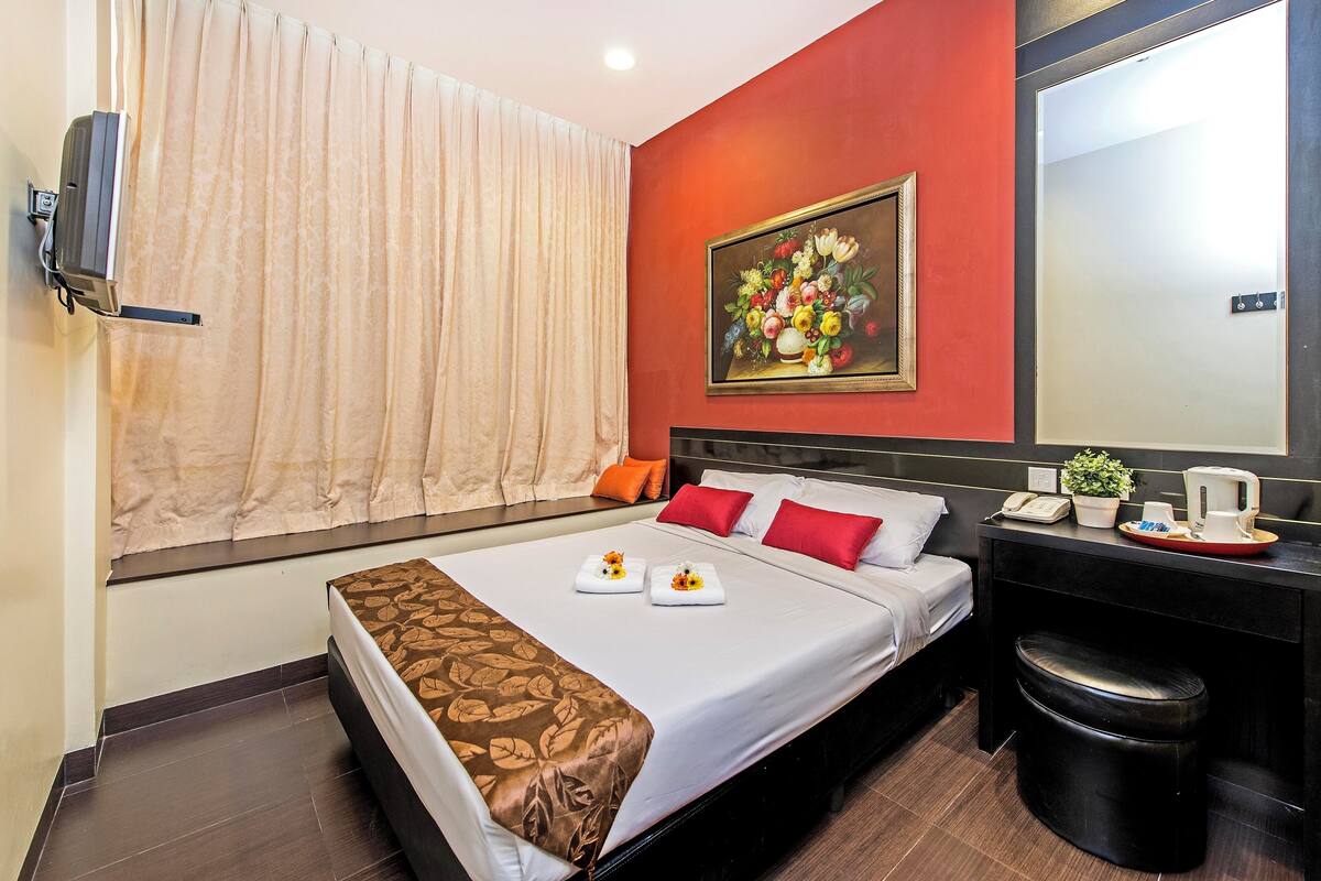 Quarto de hotel com uma cama, uma mesa com telefone e planta, um espelho e um quadro na parede.