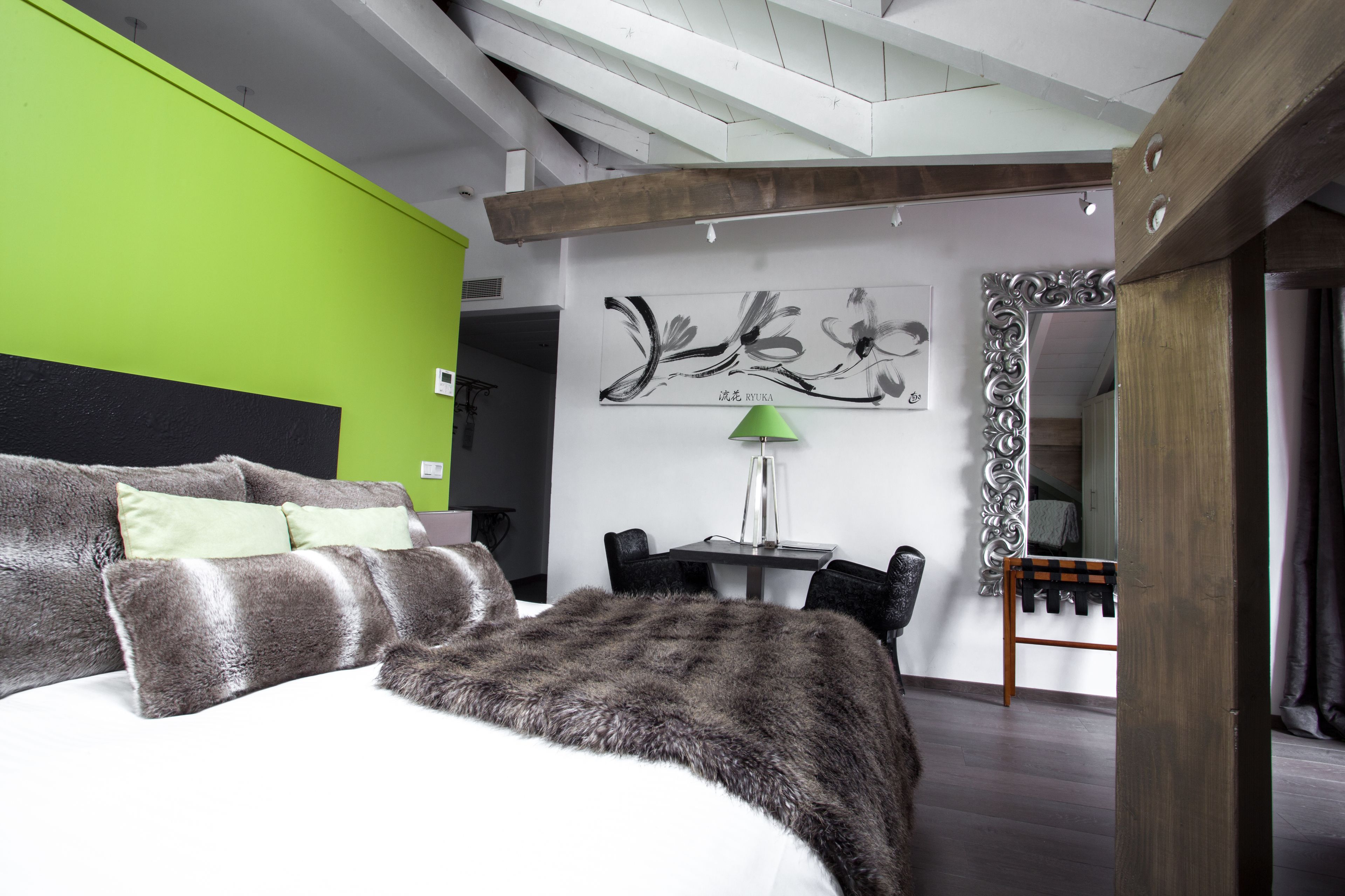 Um quarto moderno com uma cama grande, uma parede de destaque verde, teto de madeira e um espaço de jantar com mesa e cadeiras.