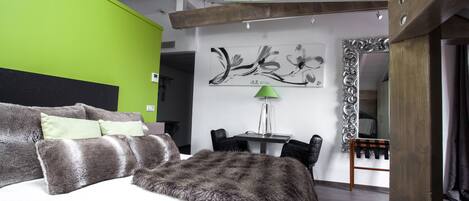 A modern bedroom with a large bed, a green accent wall, a wooden ceiling, and a dining area with a table and chairs.