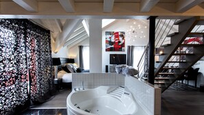 Een moderne hotelkamer met een groot bad, een trap en een zithoek met een bank en een televisie.