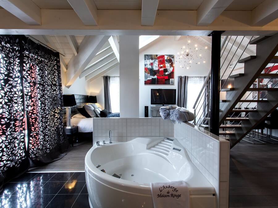 A modern hotel room with a large bathtub, a staircase, and a living area with a sofa and a TV.